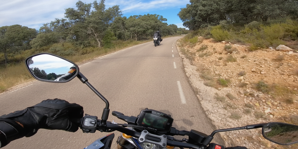 Vista desde el manillar de una moto circulando por una carretera de curvas, con otro motorista invadiendo el carril de frente